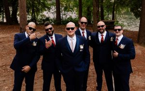 Groomsmen in navy suits and sunglasses pose together outdoors.