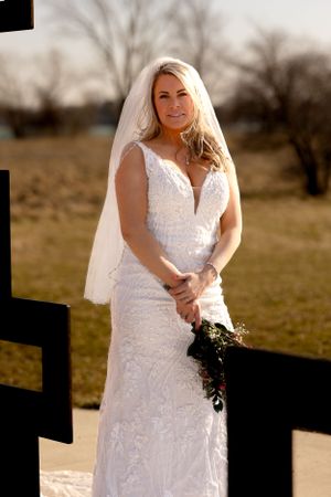 A bride in a fitted lace wedding dress poses outdoors against a rustic backdrop at sunset.