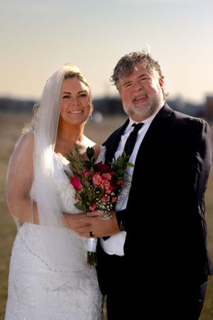 Wedding portraits at golden hour with bride holding red and pink bouquet.