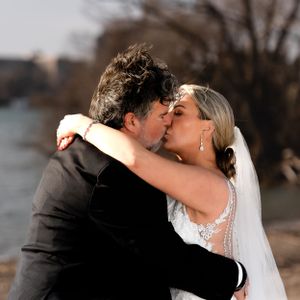 A romantic wedding kiss captured against a waterfront backdrop at sunset.