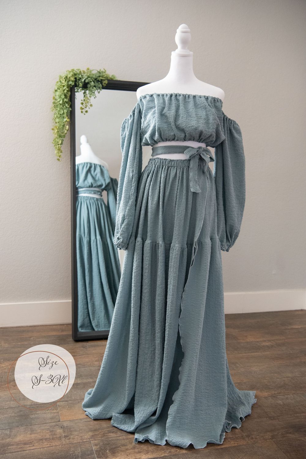 Sage green off-shoulder maxi dress with balloon sleeves and waist tie displayed in front of mirror.