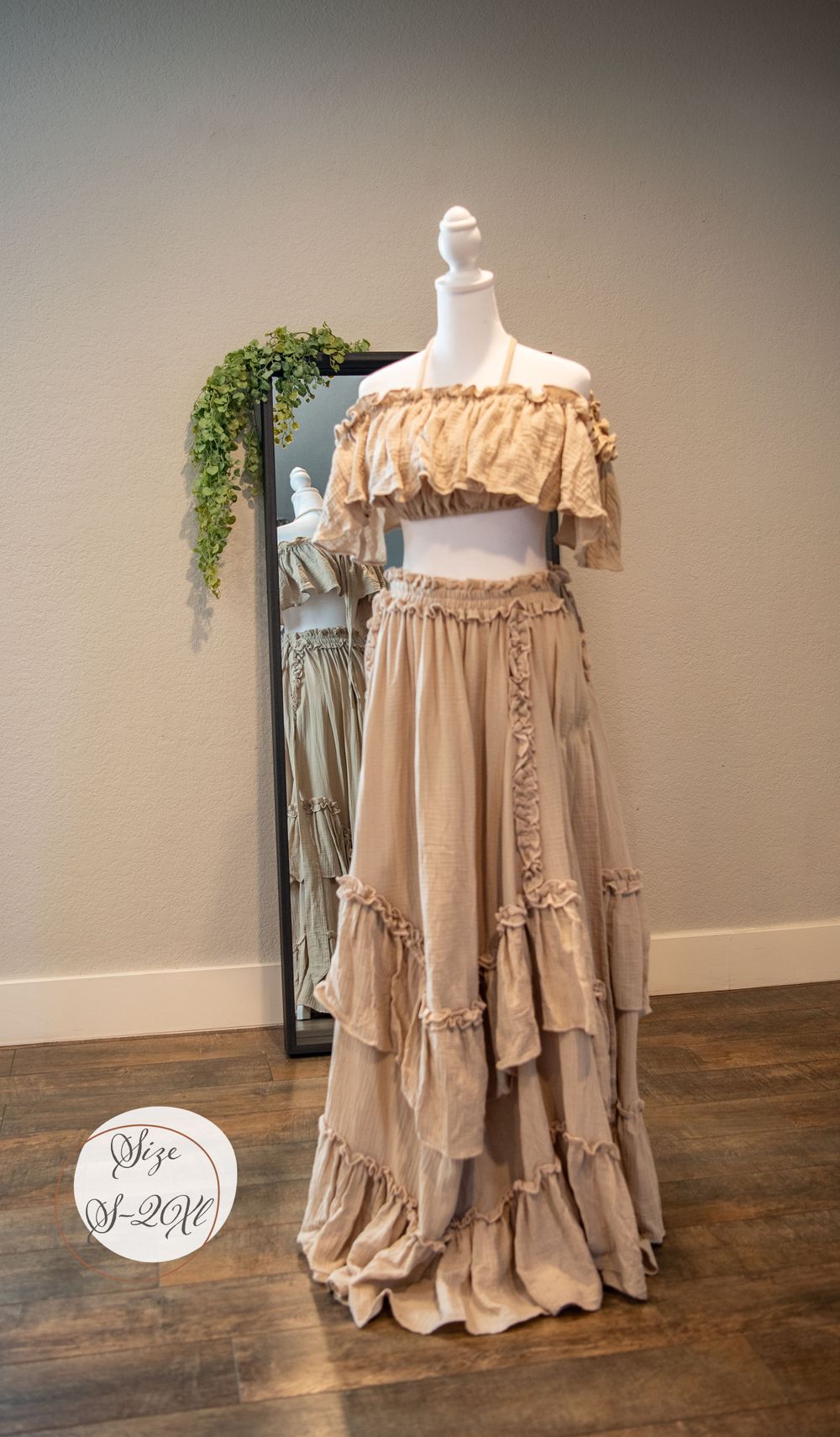 Two-piece beige ruffled dress with off-shoulder crop top and tiered maxi skirt on mannequin display.