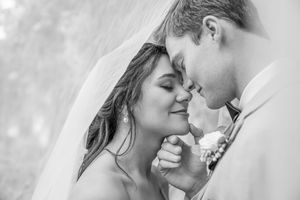 Black and white wedding photo of bride and groom sharing an intimate moment under a veil.