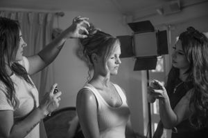 Black and white photograph of someone getting their hair styled and makeup done by two stylists during preparation.