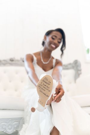 Elegant bride in white dress showing personalized wedding message written on bottom of bridal shoe.