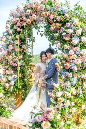 Romantic floral arch with pink roses framing couple on their wedding day.