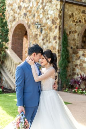 Tender wedding embrace against rustic stone wall with lush garden backdrop.