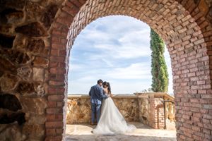 Wedding couple photographed through stone archway against blue sky.