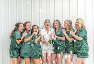 A group in matching green silk robes share a candid laughing moment together during pre-wedding preparations.
