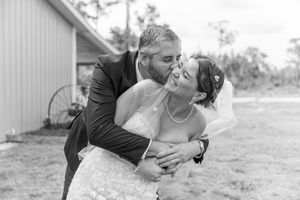 A couple in wedding attire share a joyful embrace and laugh together outdoors in black and white photography.