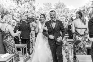 Newlyweds walk down the aisle smiling while wedding guests celebrate during an outdoor garden ceremony.