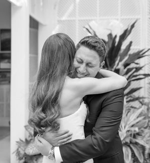 Black and white candid wedding photo of bride and groom embracing and laughing during a joyful moment in front of plants.