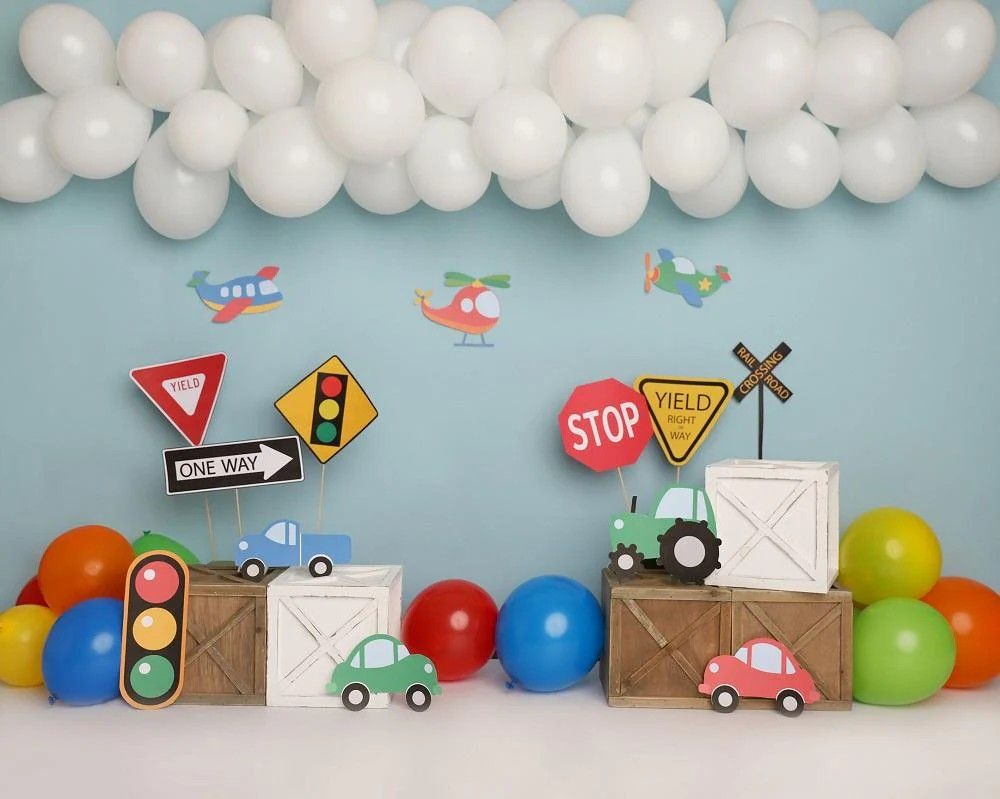 Transportation themed birthday party decorations featuring colorful balloons, road signs, and toy cars on blue background.