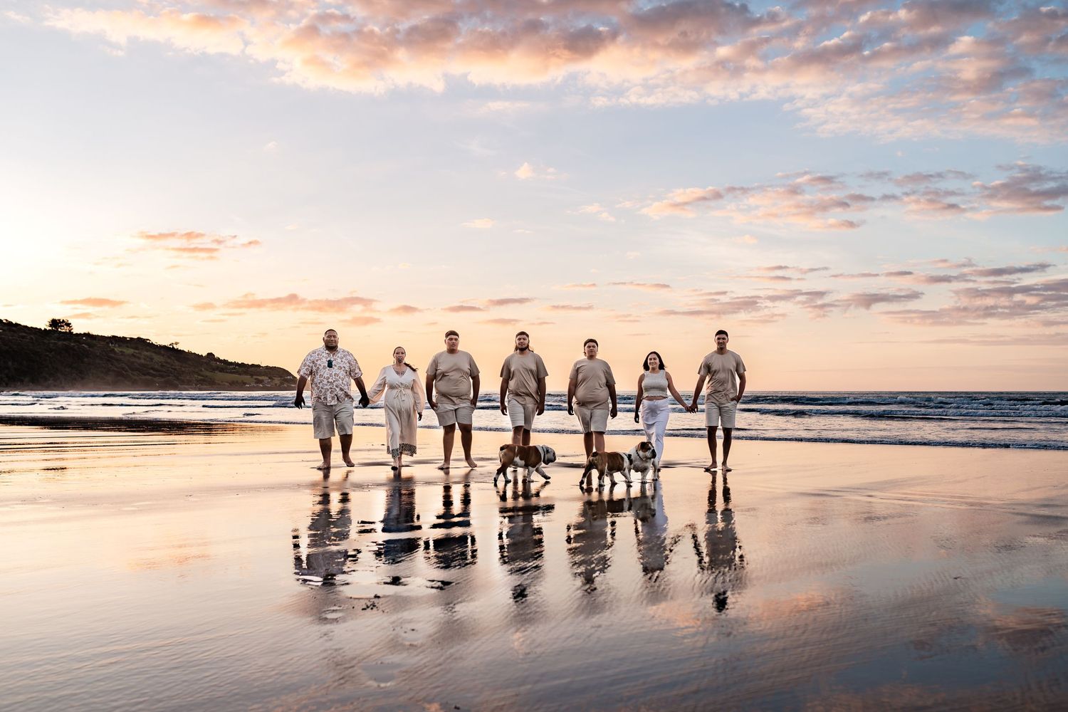 Group walking on reflective beach at sunset creating mirror images.