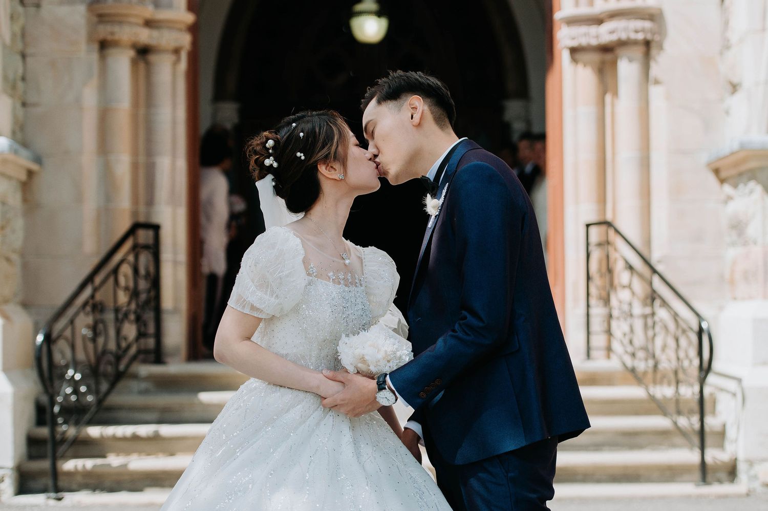 A romantic wedding couple shares a tender moment on stone steps of a historic building.