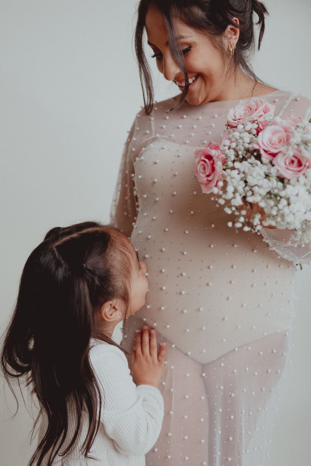 Sweet moment captured as a child touches a pregnant belly while mother holds a floral bouquet.