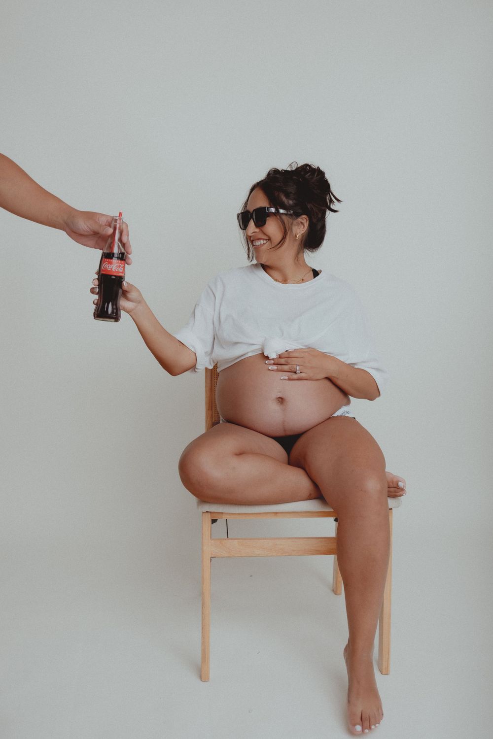 A maternity photo with someone handing over a glass bottle in a minimalist setting.