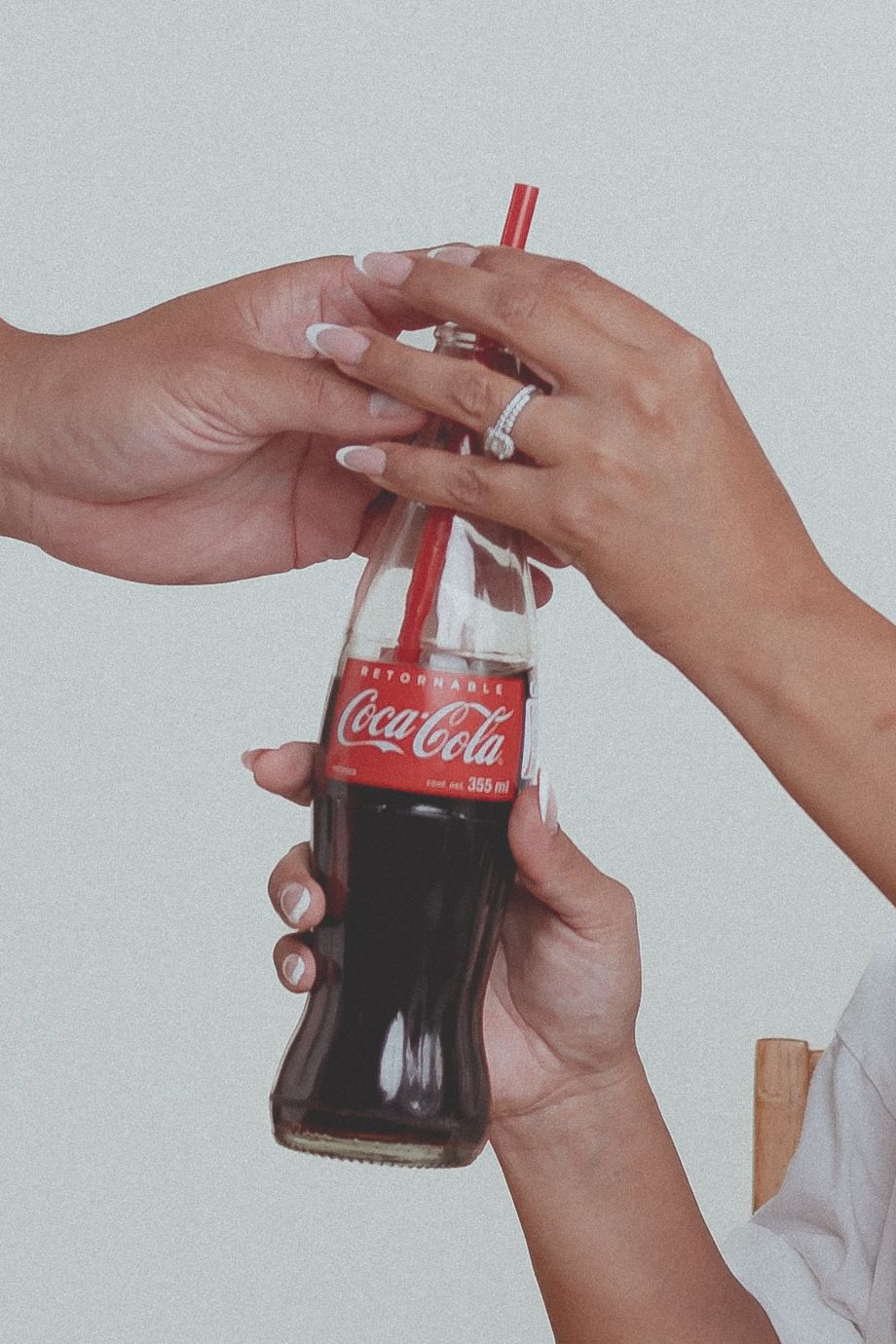 Hands wearing engagement ring hold a classic Coca-Cola bottle with red straw.