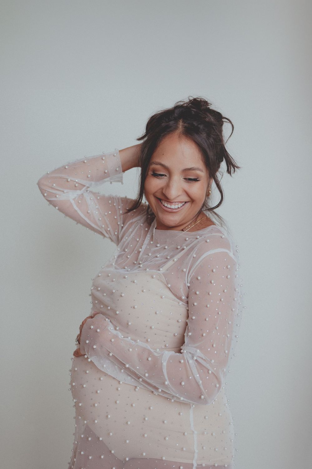 Joyful moment captured in sheer pearl-dotted dress during maternity photoshoot.