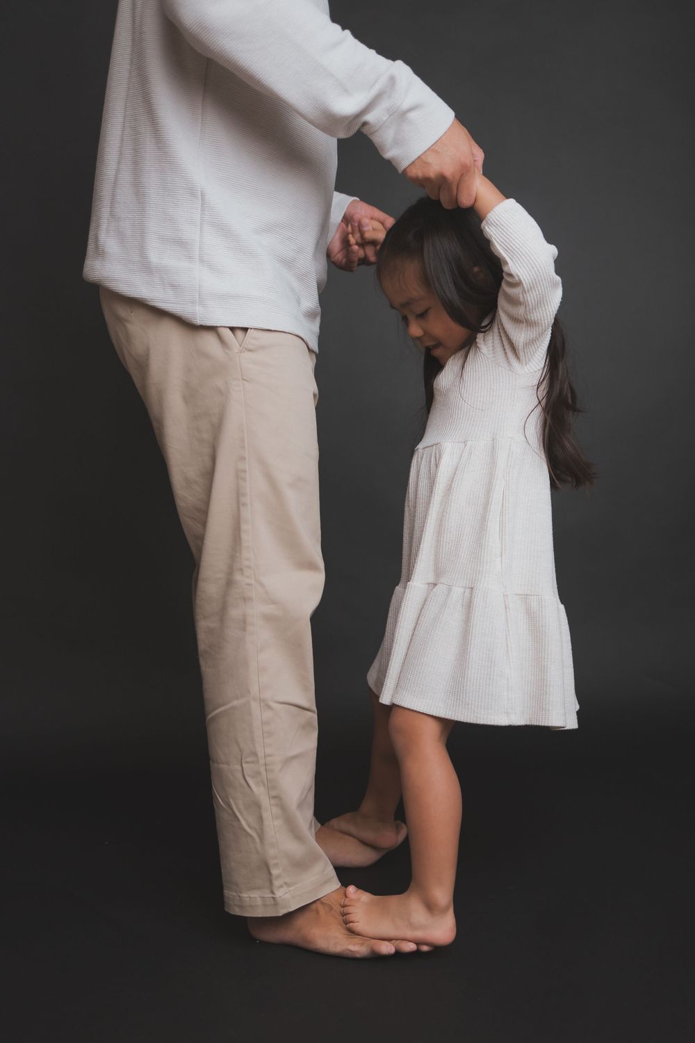 Parent and child in white clothing dance together against dark background.