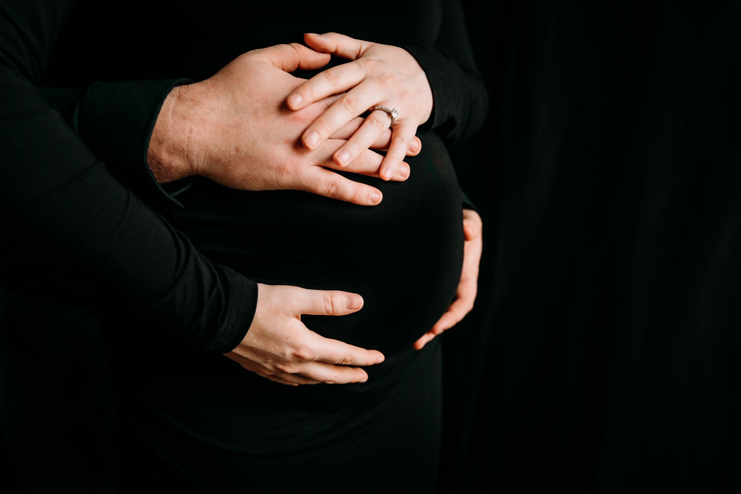 Artistic black and white maternity photos showing hands cradling a pregnant belly.