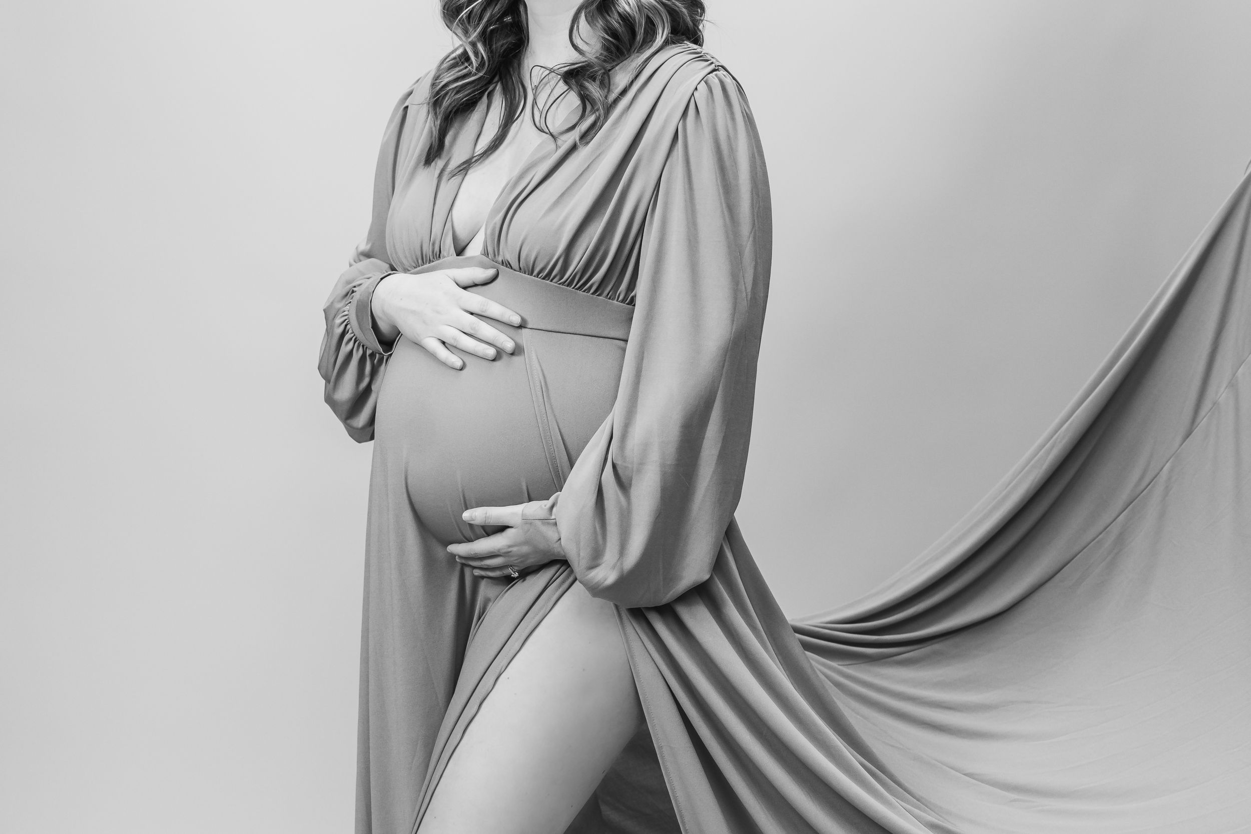 Elegant maternity photos featuring a flowing grey dress against a light background.