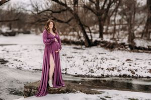 Winter maternity photoshoot in the snow with a woman wearing a flowing purple gown.