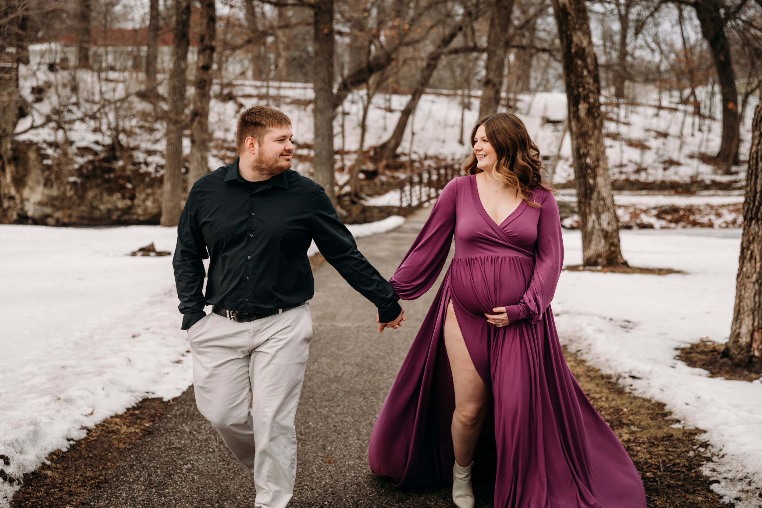 Couple walking together in a snowy winter landscape during a maternity photoshoot.