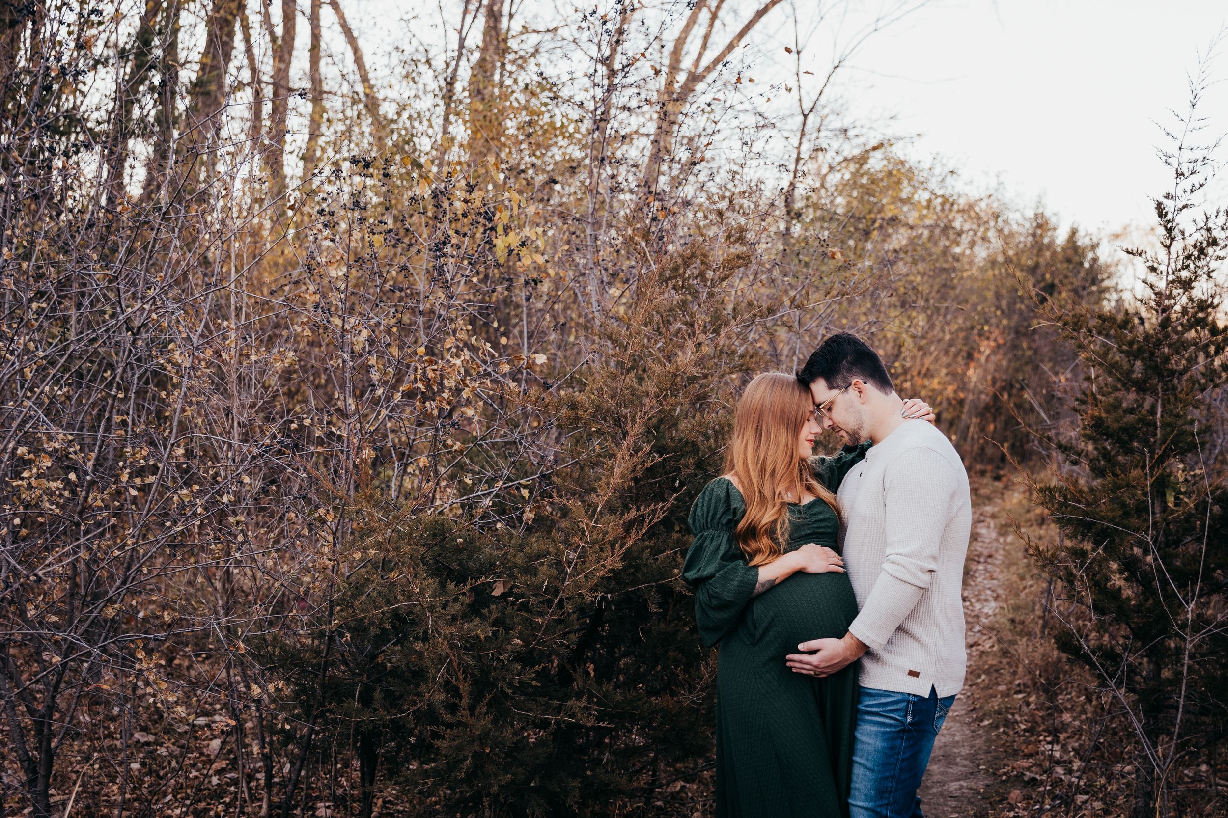 A couple embraces in a romantic autumn forest setting during golden hour.