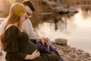 A couple sits together by a tranquil riverside during sunset.