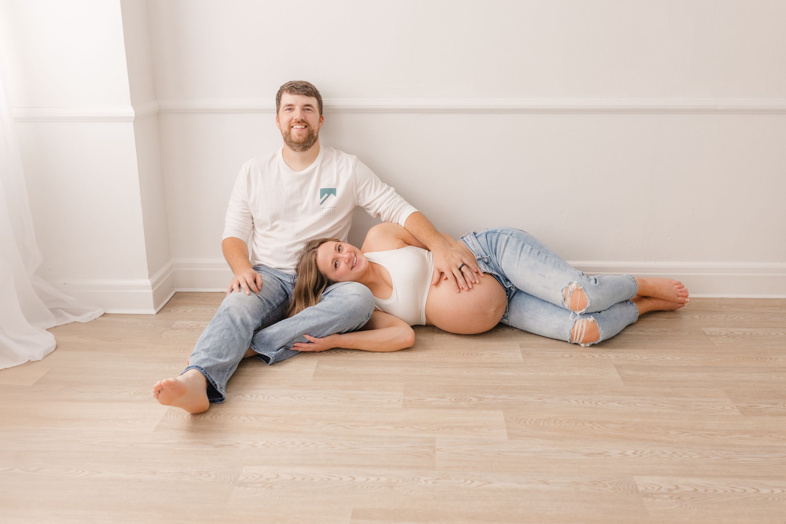 Casual lifestyle maternity photos with couple relaxing on wooden floor.