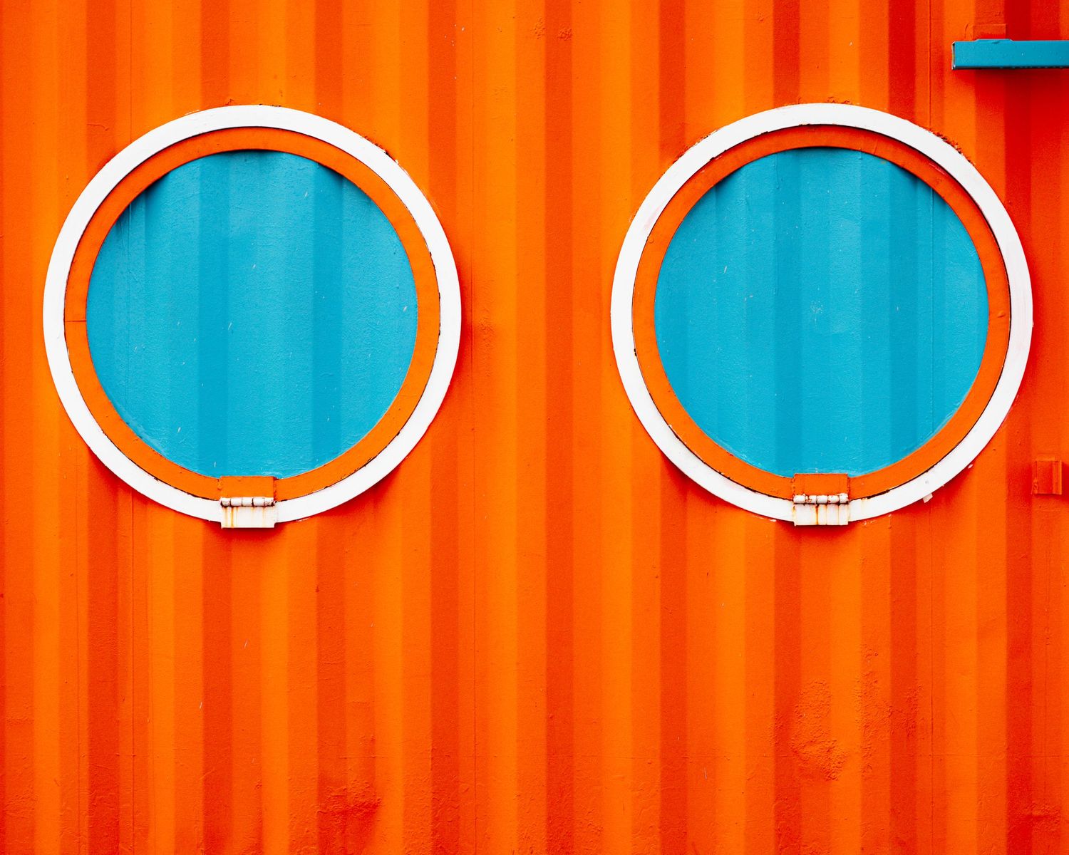 Two blue circular portholes mounted on an orange shipping container wall create a contrasting geometric pattern.