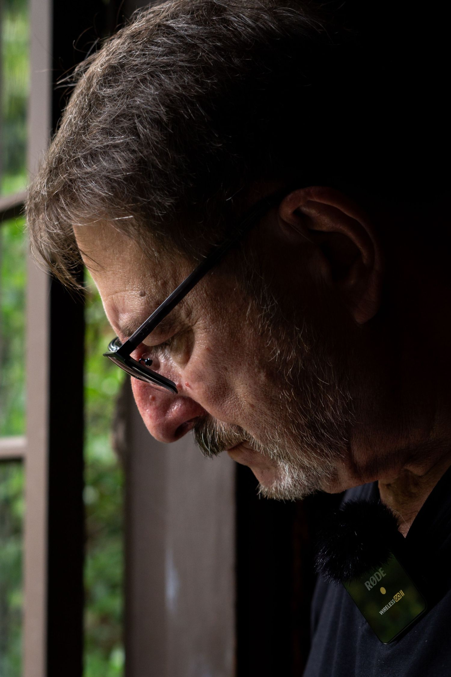 Side profile of a person with glasses looking down in dramatic lighting.
