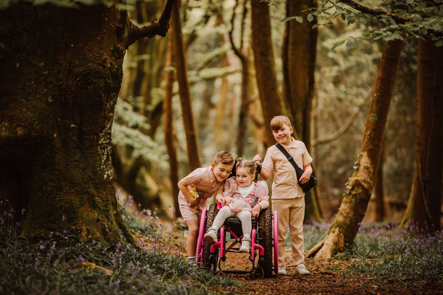 3 siblings are at Thornecombe woods Dorchester Dorset for a Bluebell photoshoot. One child is in a wheel chair. Children have SEND.