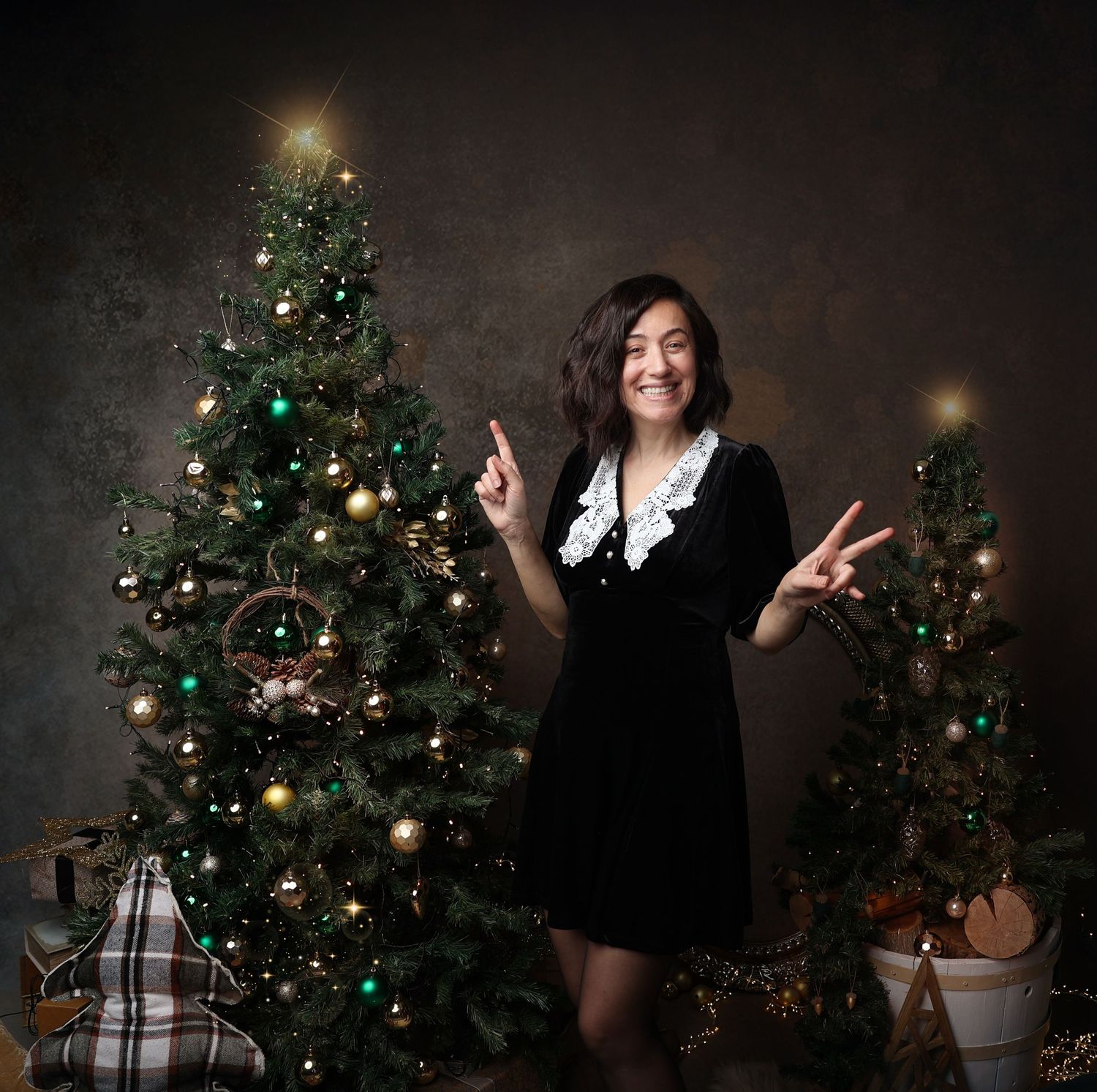 A festive holiday scene with someone posing playfully between two decorated Christmas trees.
