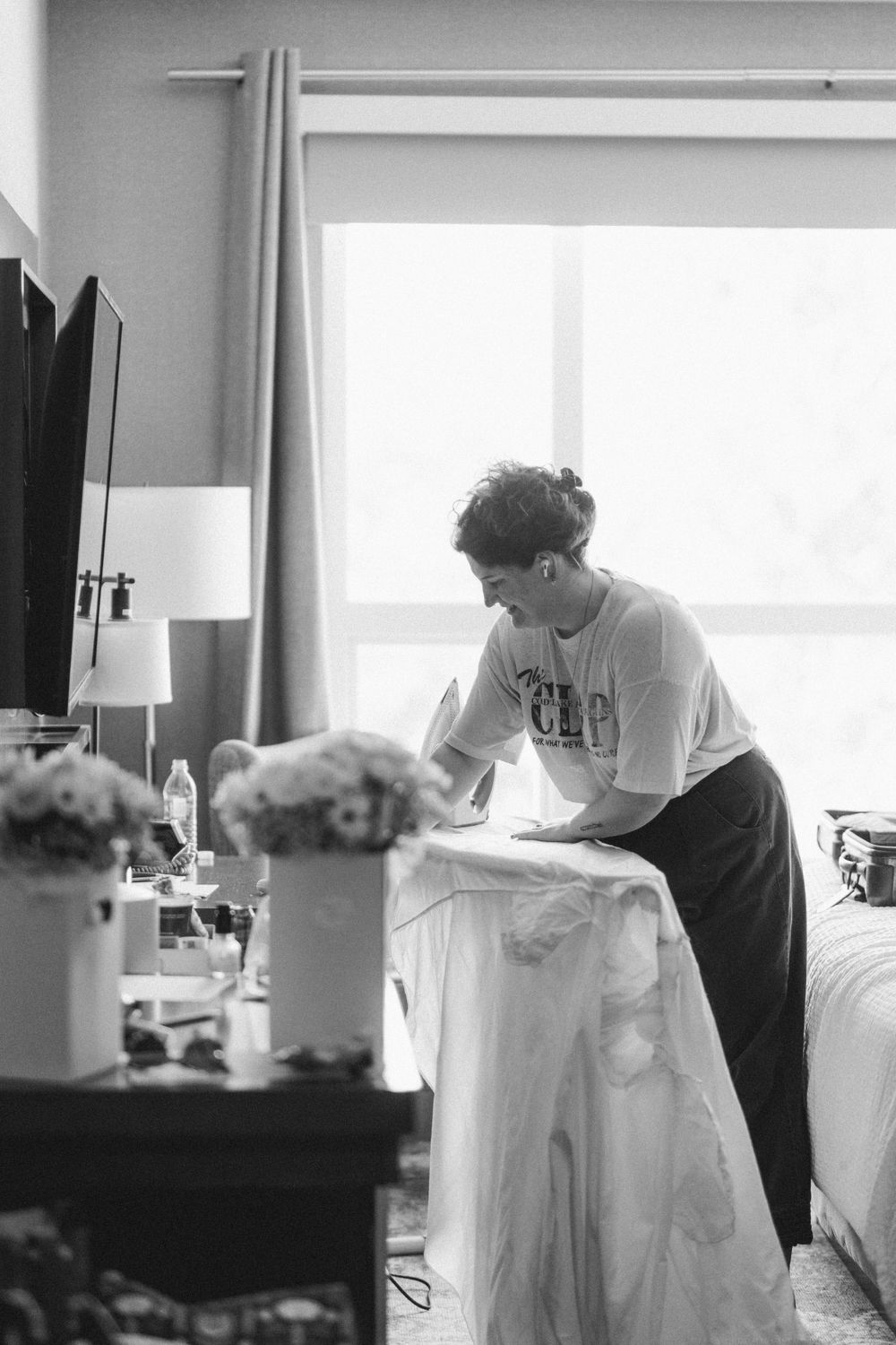 A person in casual wear tends to wedding dress preparations in a sunlit room.