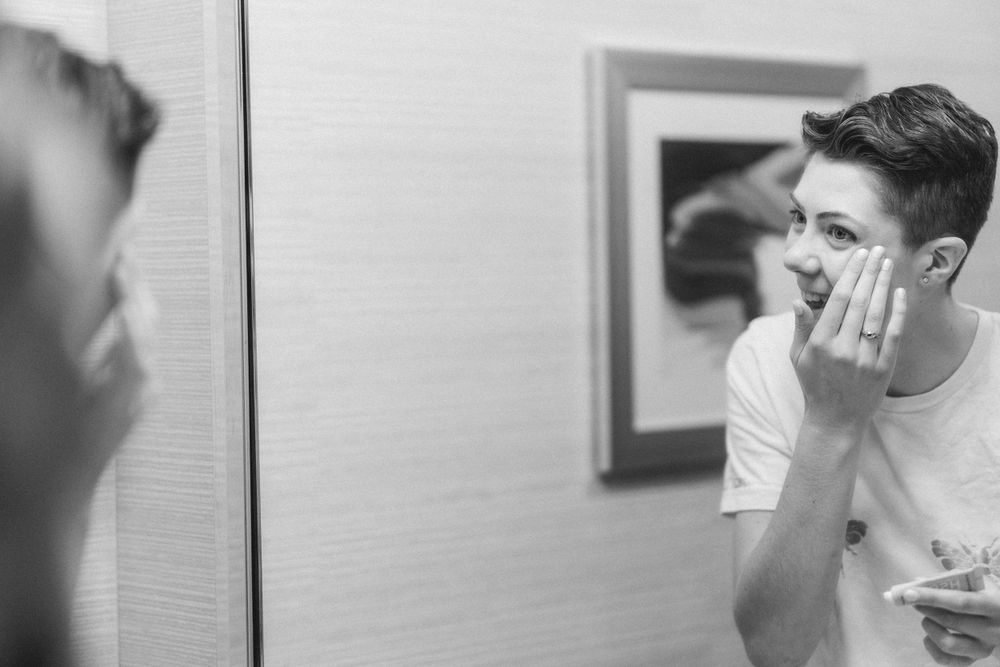 A black and white image of someone applying skincare products in a bathroom mirror.