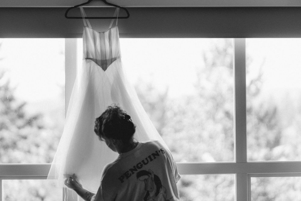A silhouette examines a white wedding dress hanging in front of a bright window.