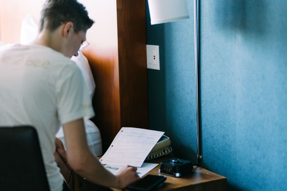 Someone reads documents while seated at a desk near a blue wall.