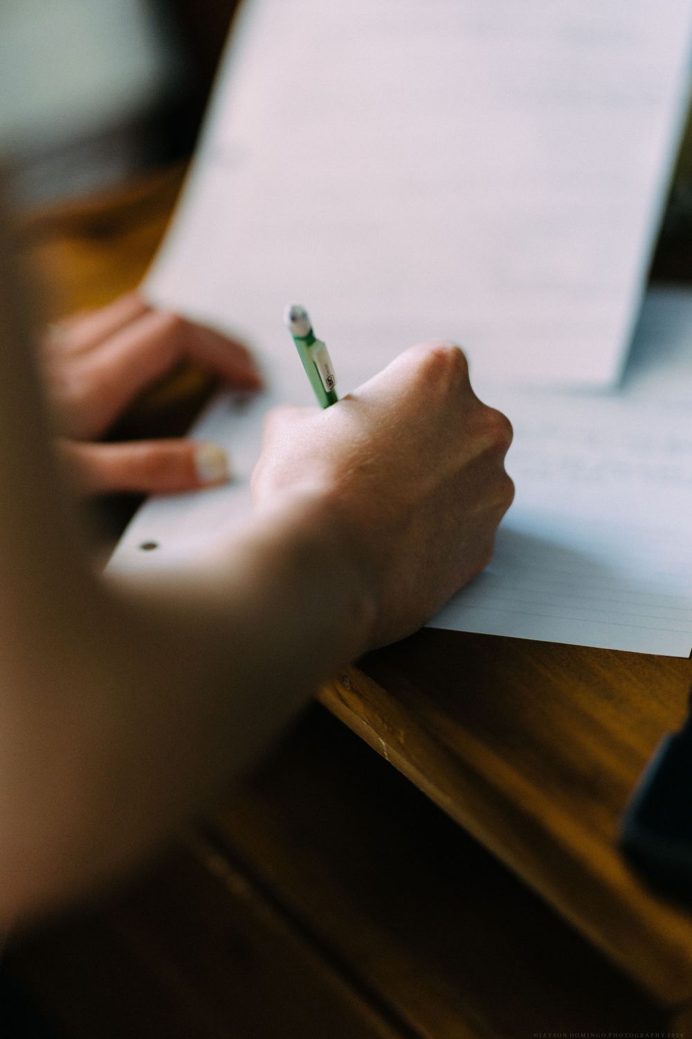 Hand holding pen while writing on paper, capturing wedding day moments.