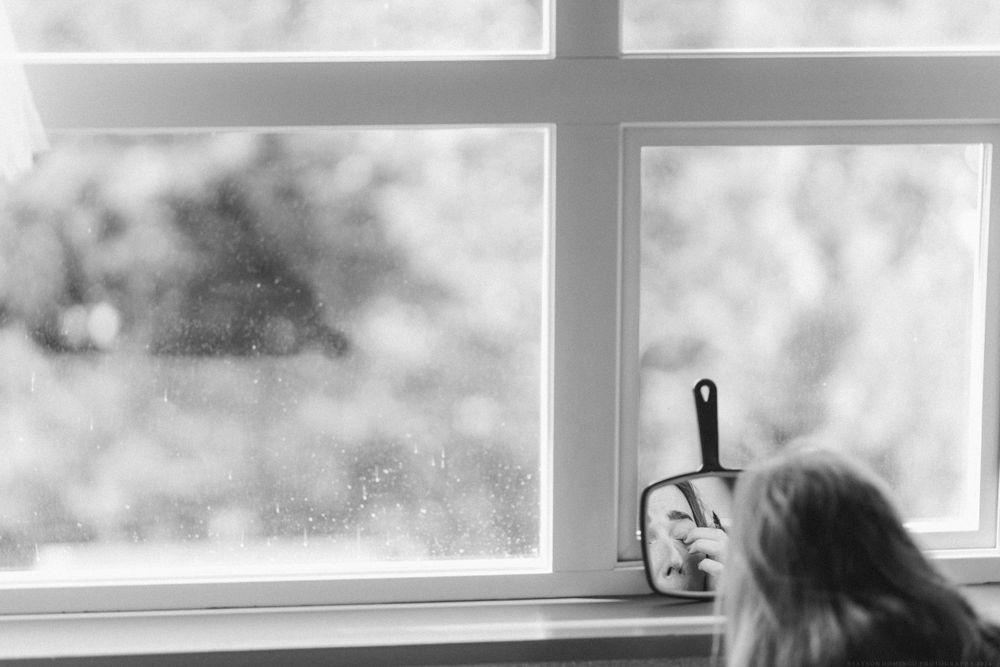 A silhouetted figure looks out a window with a pan hanging nearby.