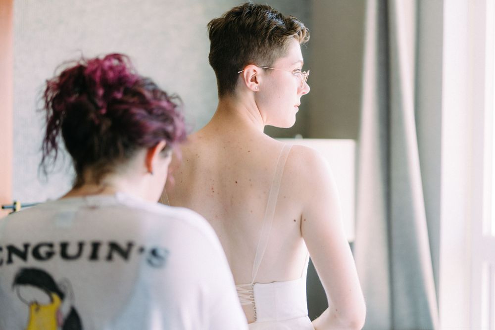 A person in a white wedding dress being helped with preparations while another wears a penguin themed shirt.