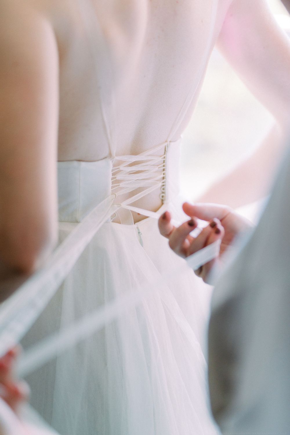 Close up view of a white wedding dress being laced up in the back.