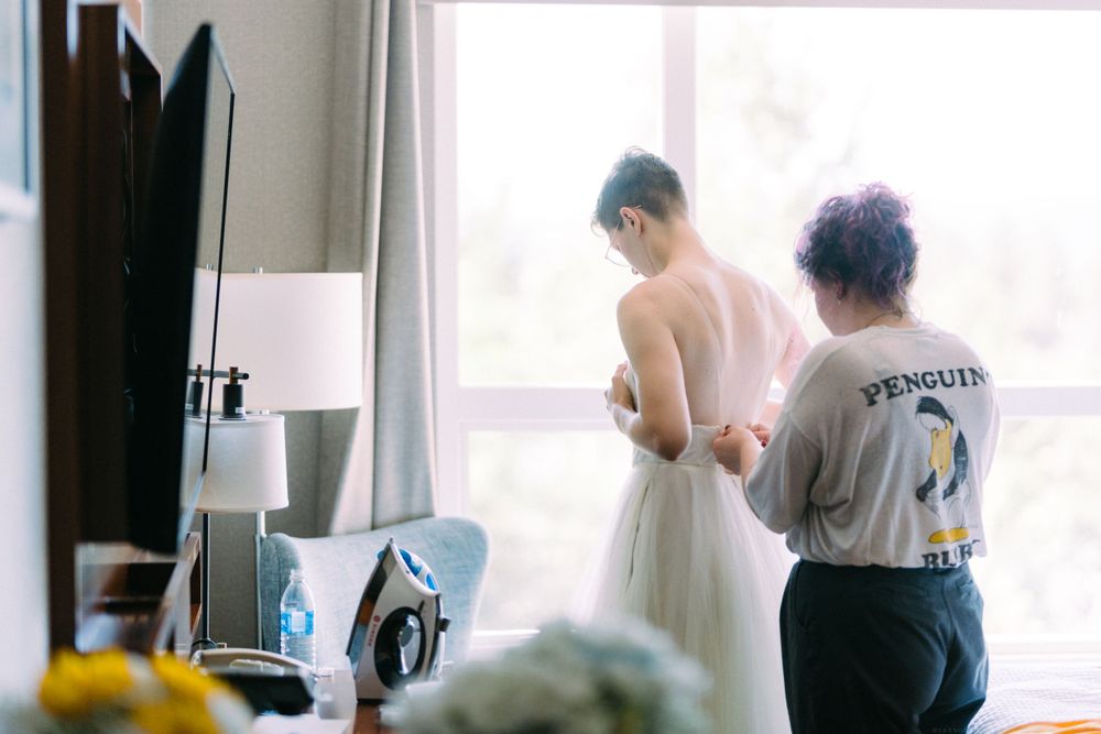 Two people stand by a window during wedding preparations, one wearing a casual penguin shirt.