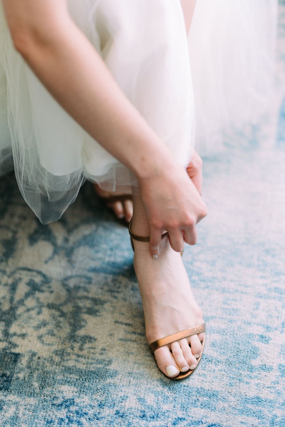 Close up of hands adjusting brown sandal straps while wearing a flowing white dress.