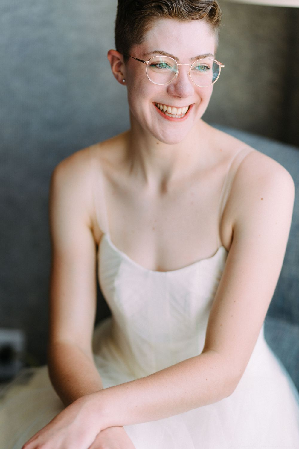Candid portrait of someone in wedding dress and glasses smiling brightly.