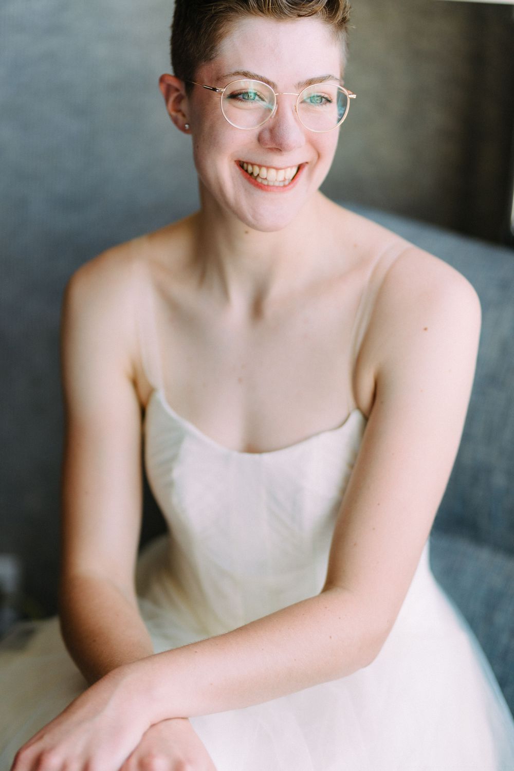 A joyful portrait of someone wearing glasses and a white dress smiling brightly.