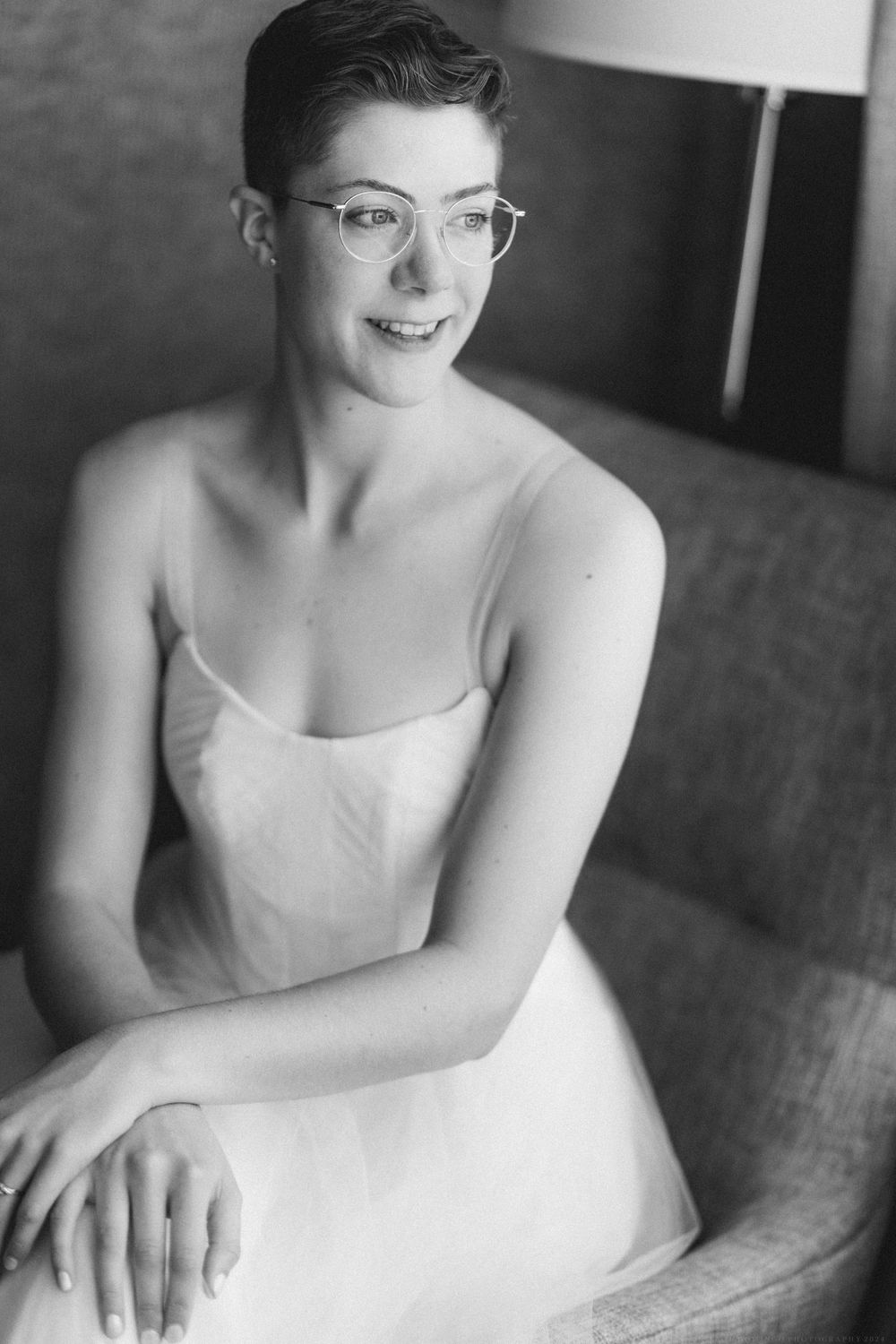 A black and white portrait showing a person in a white dress and glasses smiling warmly.