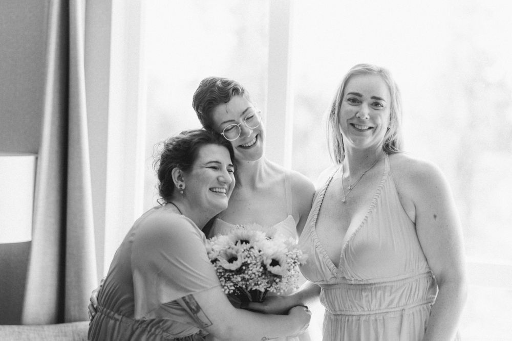 Joyful wedding party moment captured in black and white by window.