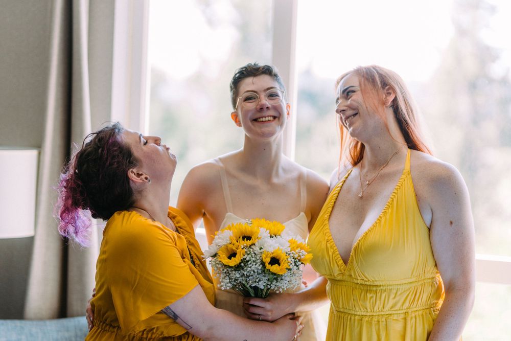 Three people in yellow and white attire share a laughing moment with sunflowers.